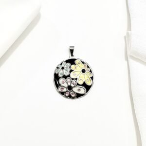 Dije redondo con flores sobre fondo de esmalte negro.