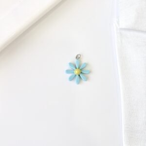 Dije flor celeste, centro amarillo. Fabricado en material plástico.