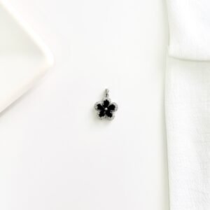 Dije flor plateada con piedras negras.